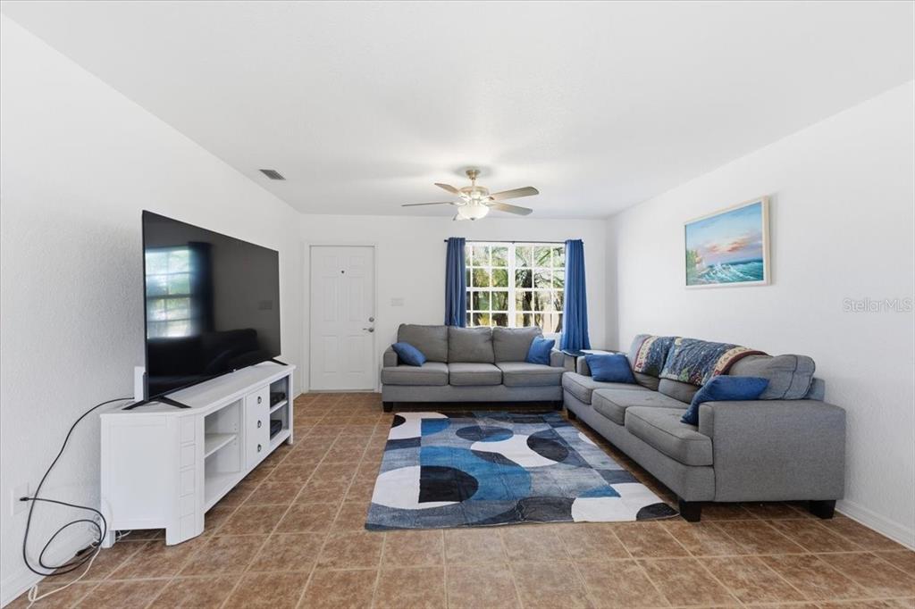 A living room features tile flooring, two gray sofas, a television, and a blue rug — 6628 THORMAN ROAD, PORT CHARLOTTE, FL