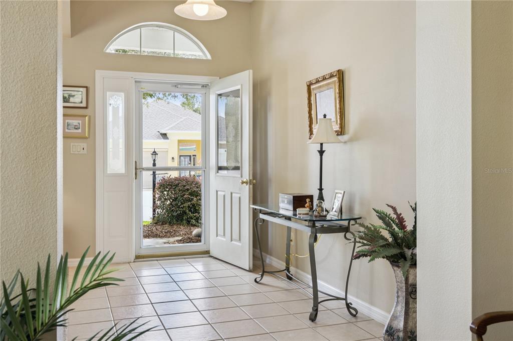 An entryway with tile flooring, a glass-topped console table, and an open front door — 24403 AMBERLEAF COURT, LEESBURG, FL