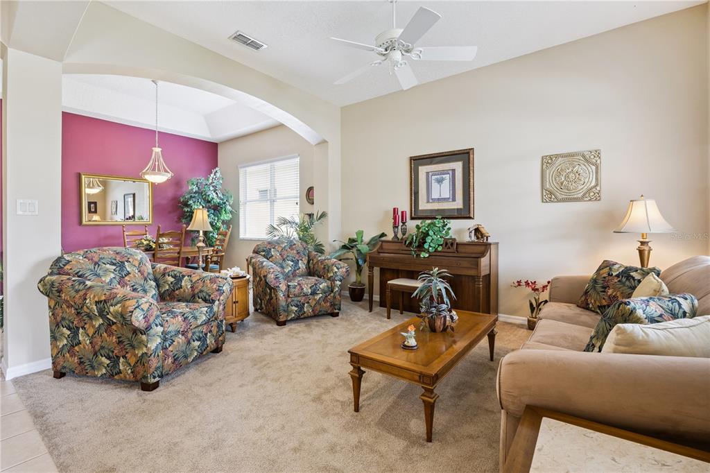 A living room features floral armchairs, a beige sofa, a wooden piano, and a dining area — 24403 AMBERLEAF COURT, LEESBURG, FL