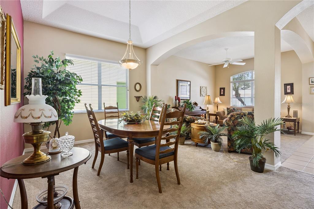 A dining area with a wooden table and chairs opens into a carpeted living room — 24403 AMBERLEAF COURT, LEESBURG, FL