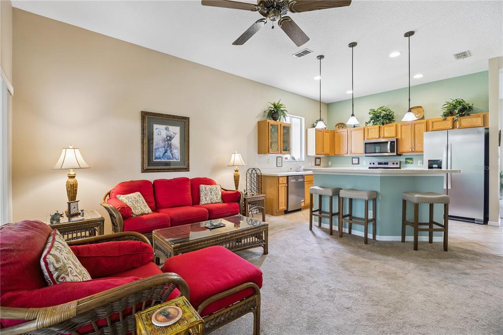 A living room with red furniture and a ceiling fan opens to a kitchen area — 24403 AMBERLEAF COURT, LEESBURG, FL