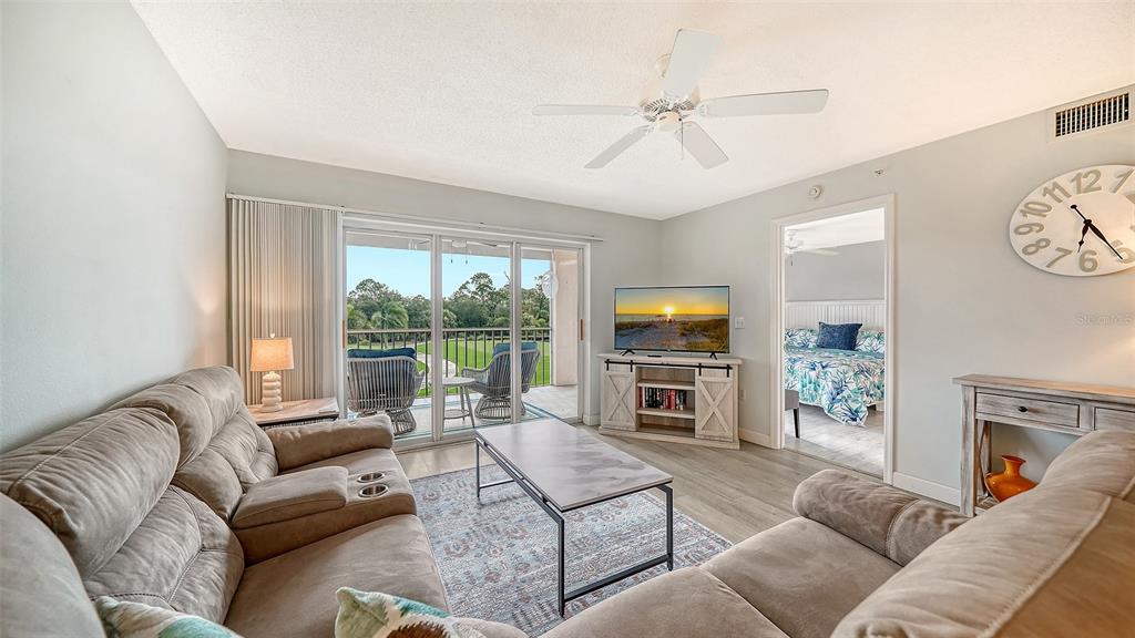 A living room features two sofas, a coffee table, a television, and a balcony view — 9320 CLUBSIDE CIRCLE UNIT 2205, SARASOTA, FL
