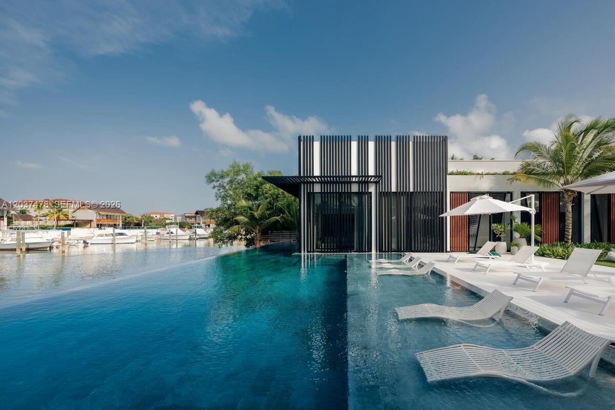 An infinity pool with submerged lounge chairs sits beside a modern building with vertical slats — 0 Marina, FL