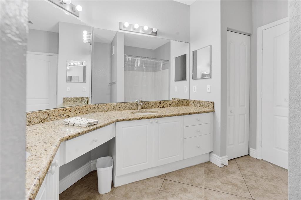 A bathroom features a granite countertop, white vanity cabinets, a large mirror, and tile flooring — 2724 VIA MURANO UNIT 638, CLEARWATER, FL