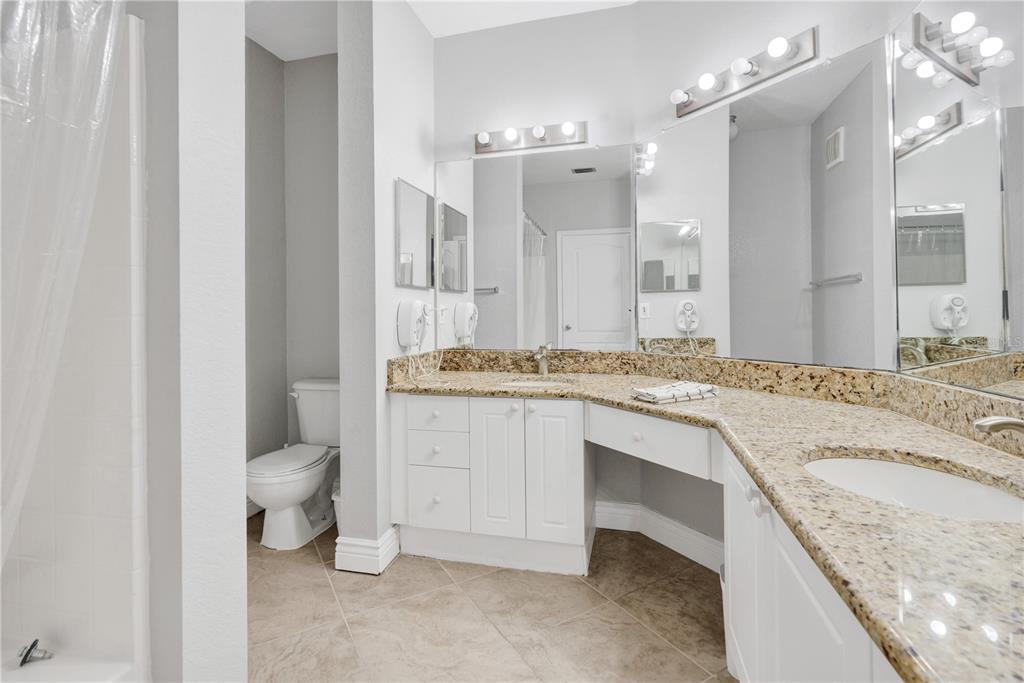 A bathroom features a granite vanity with dual sinks, white cabinets, and a toilet area — 2724 VIA MURANO UNIT 638, CLEARWATER, FL