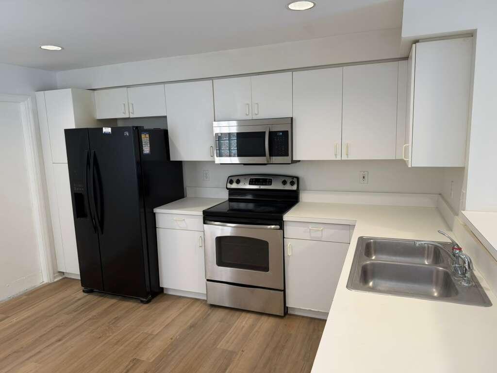 A kitchen featuring white cabinets, stainless steel appliances, a black refrigerator, and light wood flooring — 1348 Veracruz Lane # 8, Weston FL 33327, WESTON, FL