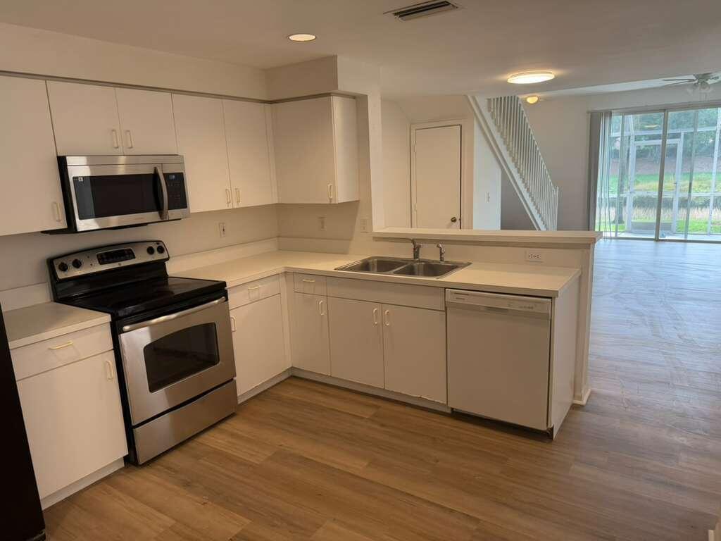 A kitchen with white cabinets, stainless steel appliances, and light wood-look flooring — 1348 Veracruz Lane # 8, Weston FL 33327, WESTON, FL