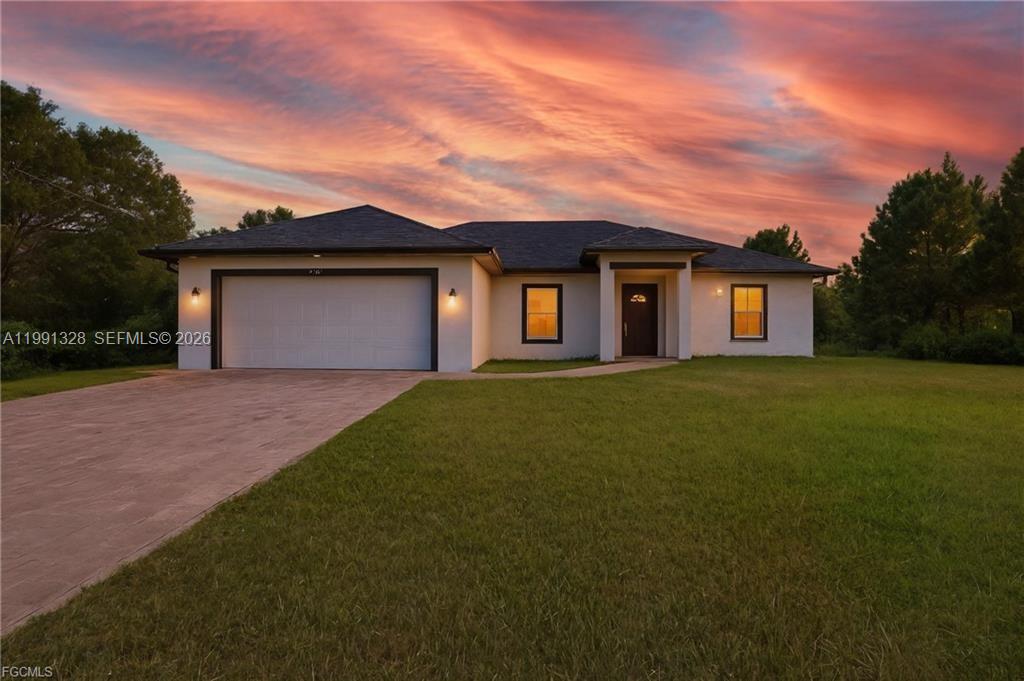 A single-story house with a two-car garage and a paved driveway at sunset — 1013 ATHERTON AVE, Lehigh Acres FL 33971, LEHIGH ACRES, FL
