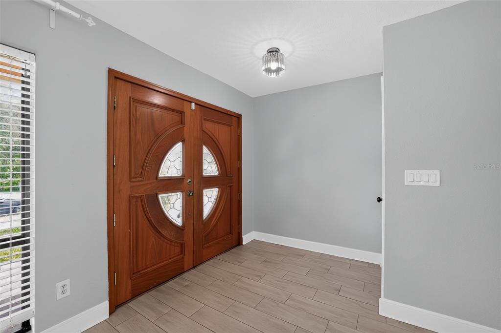 An entryway features light gray walls, wood-look tile flooring, and a double wooden front door — 7001 BAYWOOD COURT, TAMPA, FL