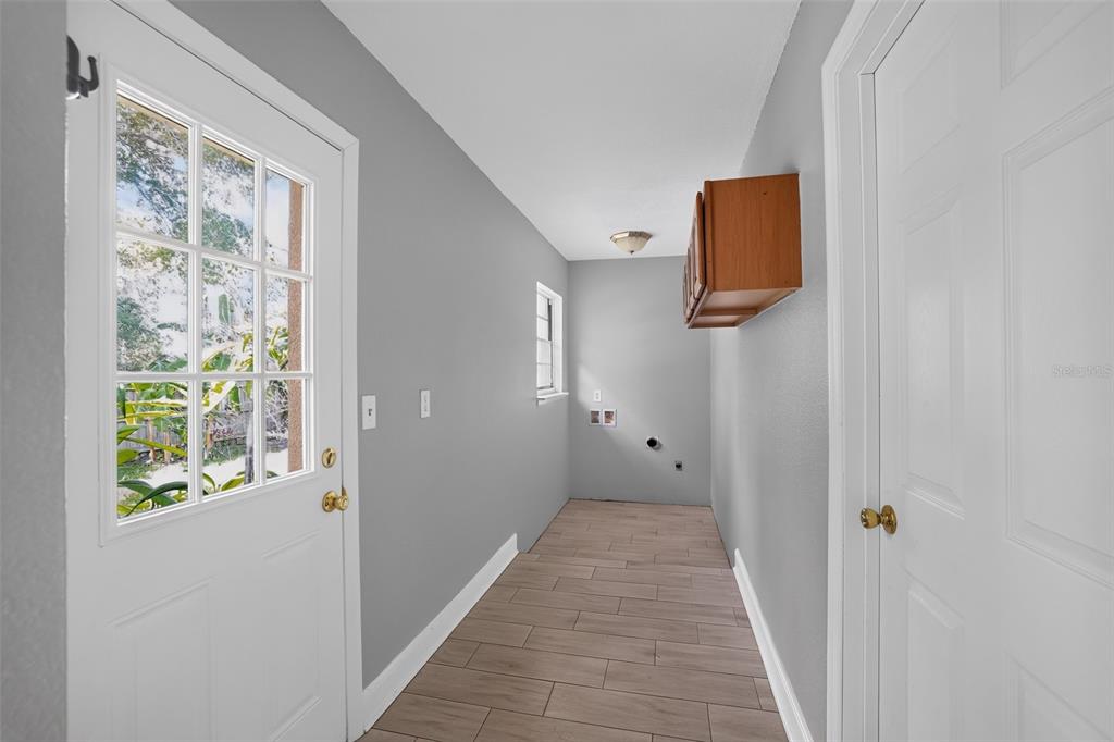 A laundry room features gray walls, wood-look tile flooring, a white door, and wall-mounted cabinetry — 7001 BAYWOOD COURT, TAMPA, FL