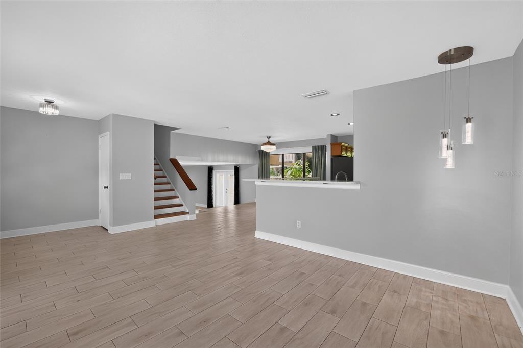 A living area with light wood-look tile flooring, a staircase, and a kitchen breakfast bar — 7001 BAYWOOD COURT, TAMPA, FL