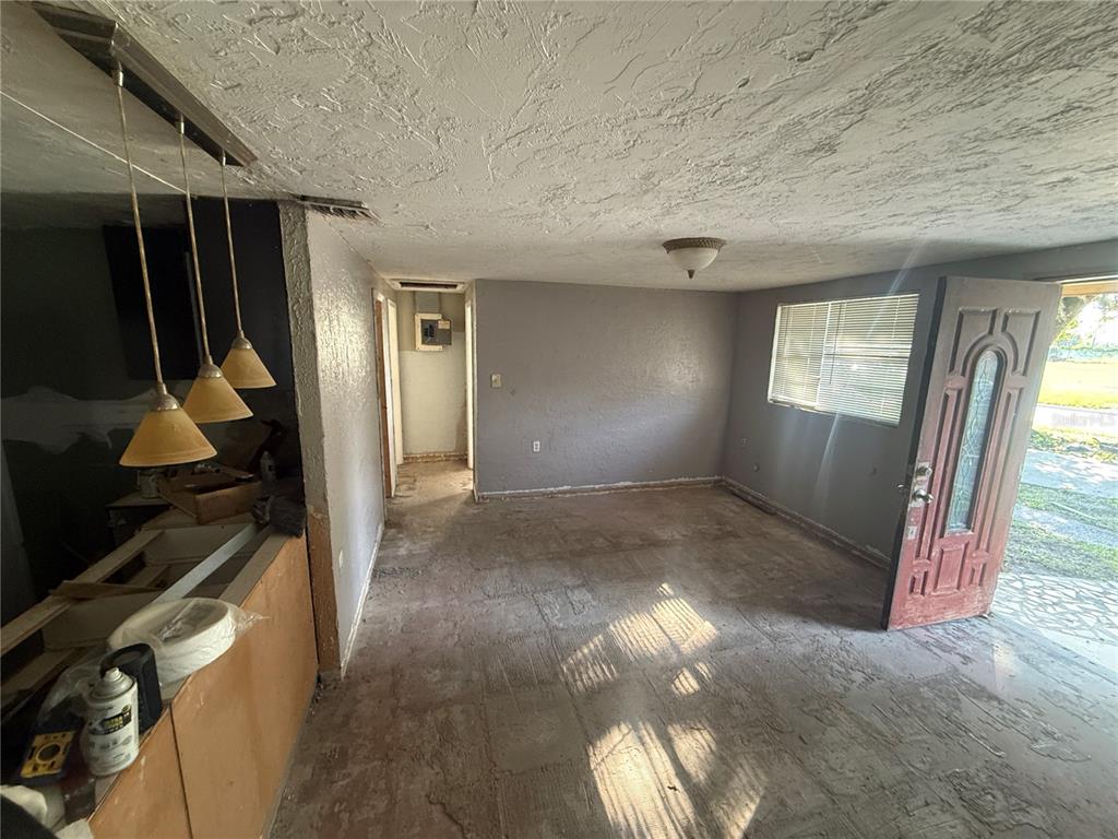 An unfinished room features gray walls, a textured ceiling, pendant lights, and an open front door — 608 S ORANGE AVENUE, ARCADIA, FL