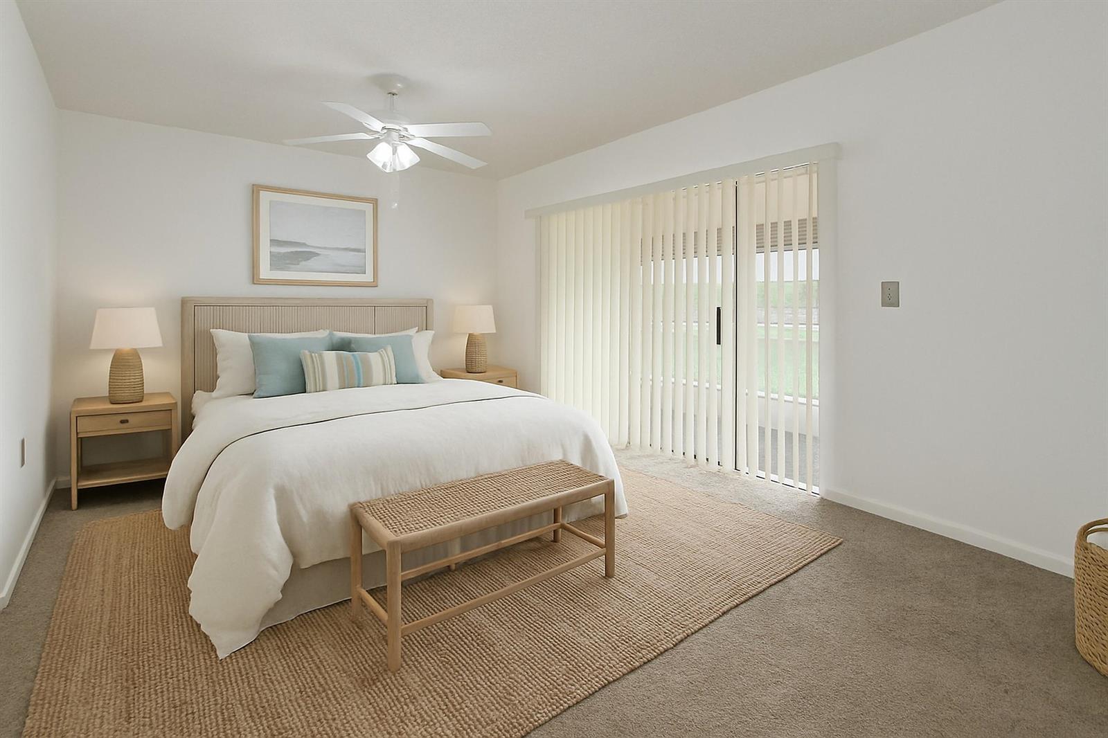 A bedroom features a bed with light blue pillows, a woven bench, and sliding glass doors — 6670 Royal Palm Boulevard # 314k, Margate FL 33063, MARGATE, FL