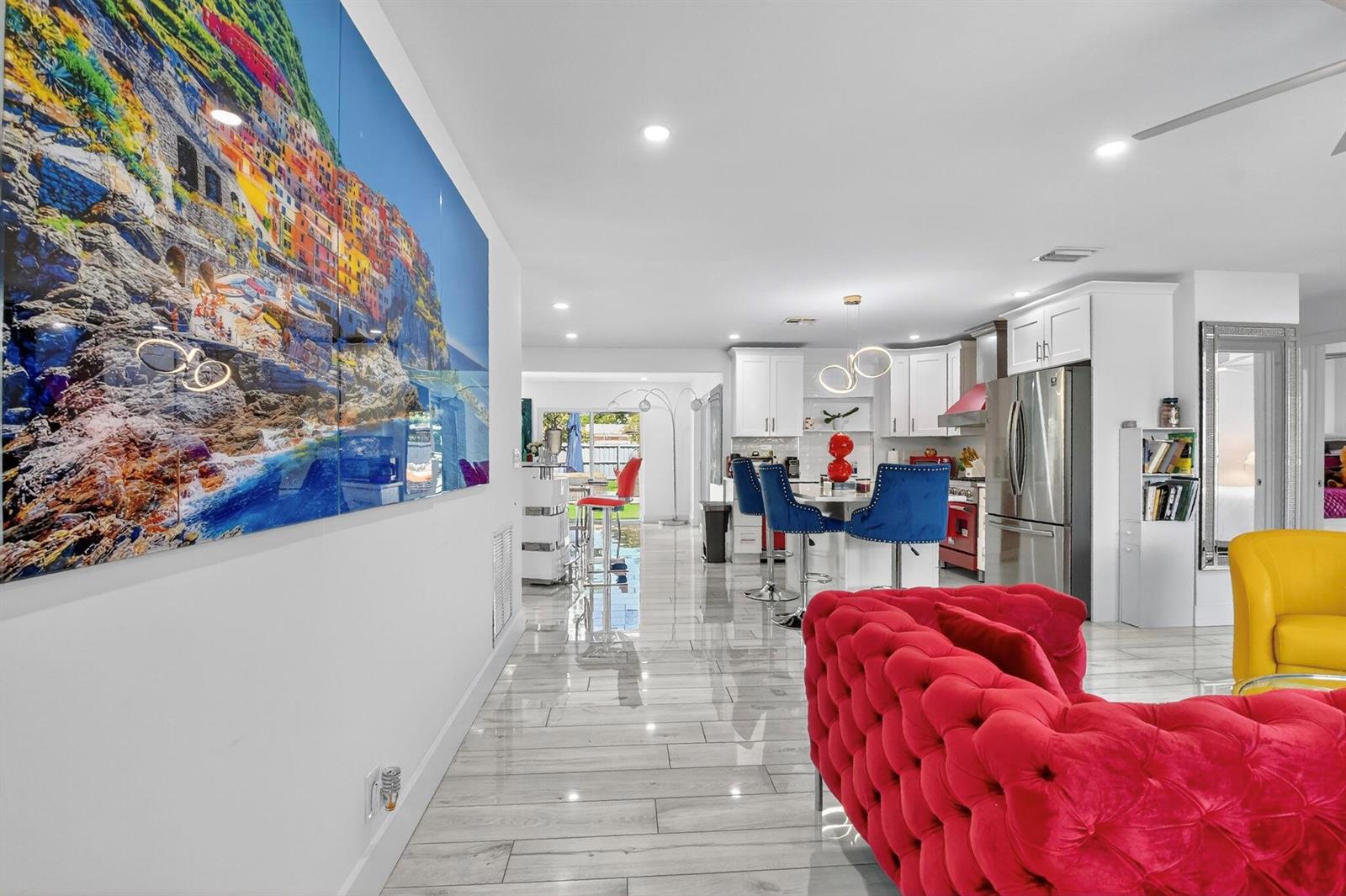 An open-concept living area features a red tufted sofa, white kitchen cabinetry, and tile flooring — 449 SW 4th Avenue, Boynton Beach FL 33435, BOYNTON BEACH, FL