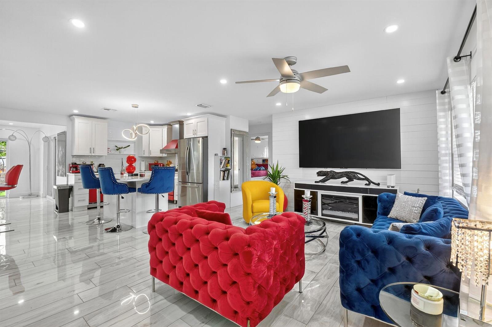 A bright open-concept living room and kitchen featuring colorful tufted furniture and tiled floors — 449 SW 4th Avenue, Boynton Beach FL 33435, BOYNTON BEACH, FL