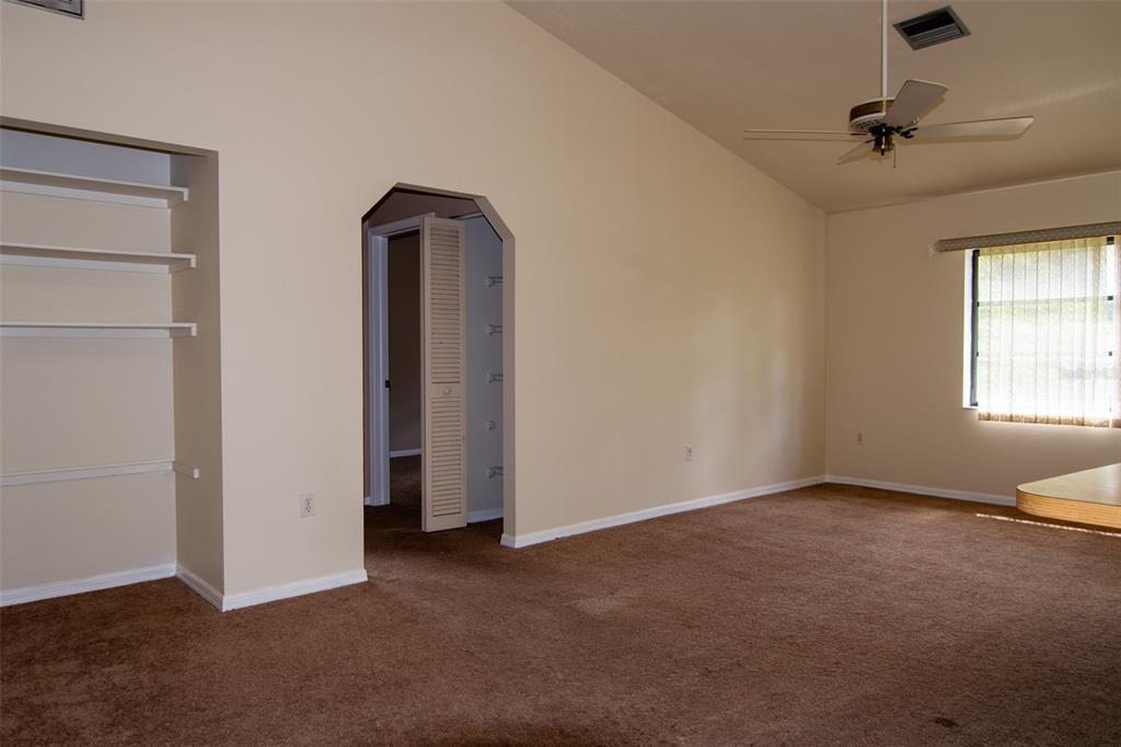 An empty room with brown carpet, beige walls, built-in shelves, and a ceiling fan — 1565 DORCHESTER STREET, PORT CHARLOTTE, FL