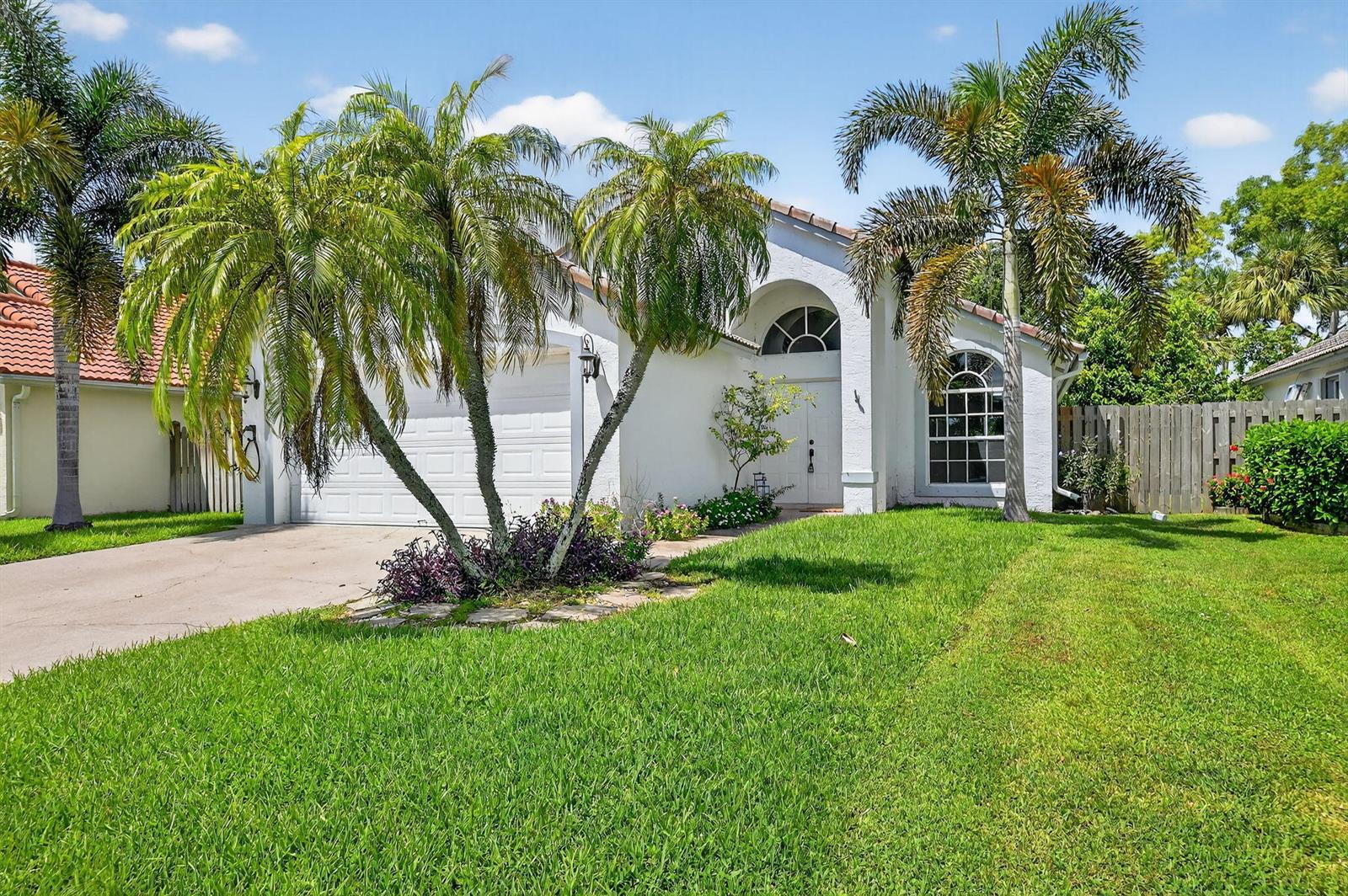 A white single-story house with a two-car garage, palm trees, and a grassy front yard — 1891 Oak Berry Circle, Wellington FL 33414, WELLINGTON, FL