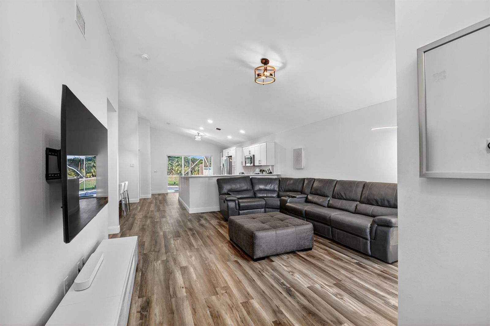 A living room with wood-look flooring, a grey sectional sofa, and an open-concept kitchen — 1891 Oak Berry Circle, Wellington FL 33414, WELLINGTON, FL