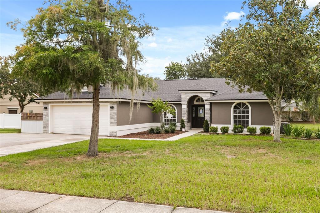 A single-story house with a two-car garage, gray stucco exterior, and stone accents — 13031 SCOTTISH PINE LANE, CLERMONT, FL