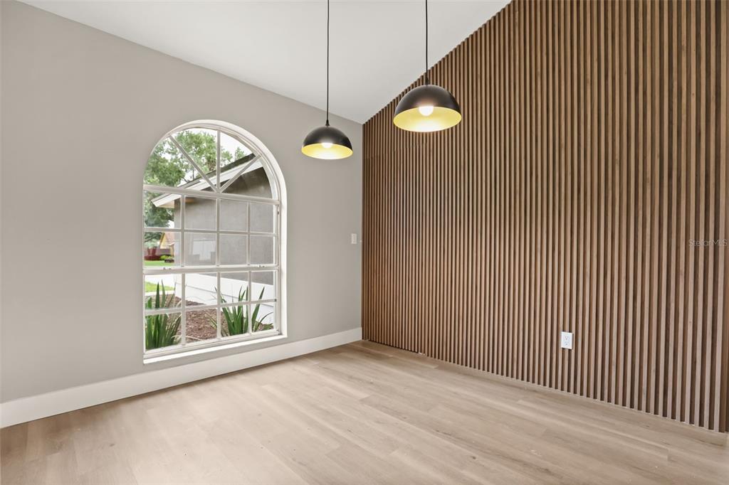 A room with light wood flooring, a large arched window, and a slatted wood accent wall — 13031 SCOTTISH PINE LANE, CLERMONT, FL