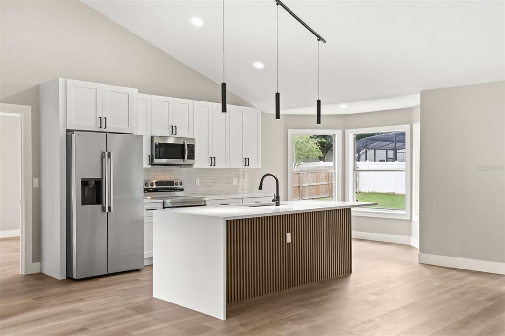 A modern kitchen features white cabinets, stainless steel appliances, and a slatted wood kitchen island — 13031 SCOTTISH PINE LANE, CLERMONT, FL