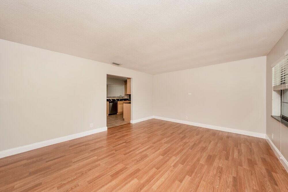 An empty living room features light-colored walls, white baseboards, and wood-look laminate flooring — BOCA RATON, FL