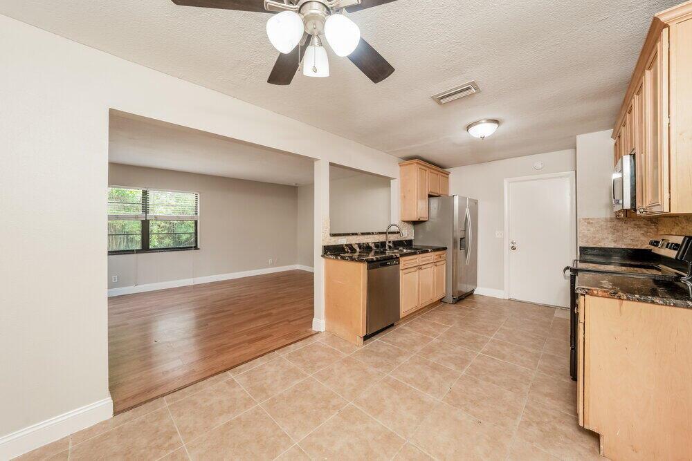 A kitchen with light wood cabinets and dark countertops opens into a living area — BOCA RATON, FL