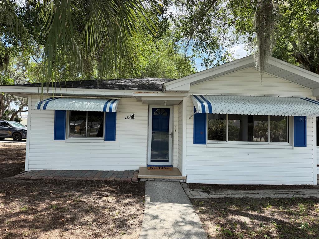 A white single-story house with blue shutters, striped awnings, and a front walkway — 301 S SEMINOLE AVENUE, MINNEOLA, FL