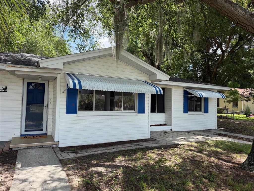 A white house with blue shutters and striped metal awnings sits under large trees — 301 S SEMINOLE AVENUE, MINNEOLA, FL