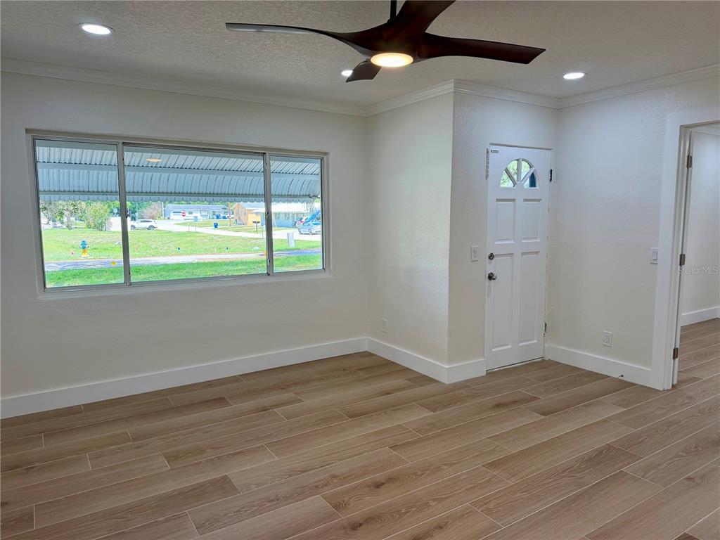 An empty room features light wood-look tile flooring, a ceiling fan, and a large window — 301 S SEMINOLE AVENUE, MINNEOLA, FL
