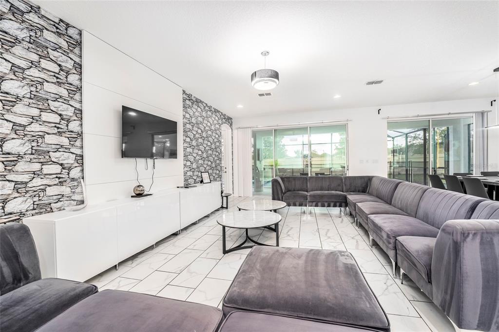A living room features a stone accent wall, white cabinetry, tile flooring, and a sectional sofa — 2613 CALISTOGA AVENUE, KISSIMMEE, FL