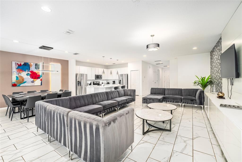 An open-concept living and dining area features gray velvet sectionals, marble-look tile flooring, and white cabinetry — 2613 CALISTOGA AVENUE, KISSIMMEE, FL