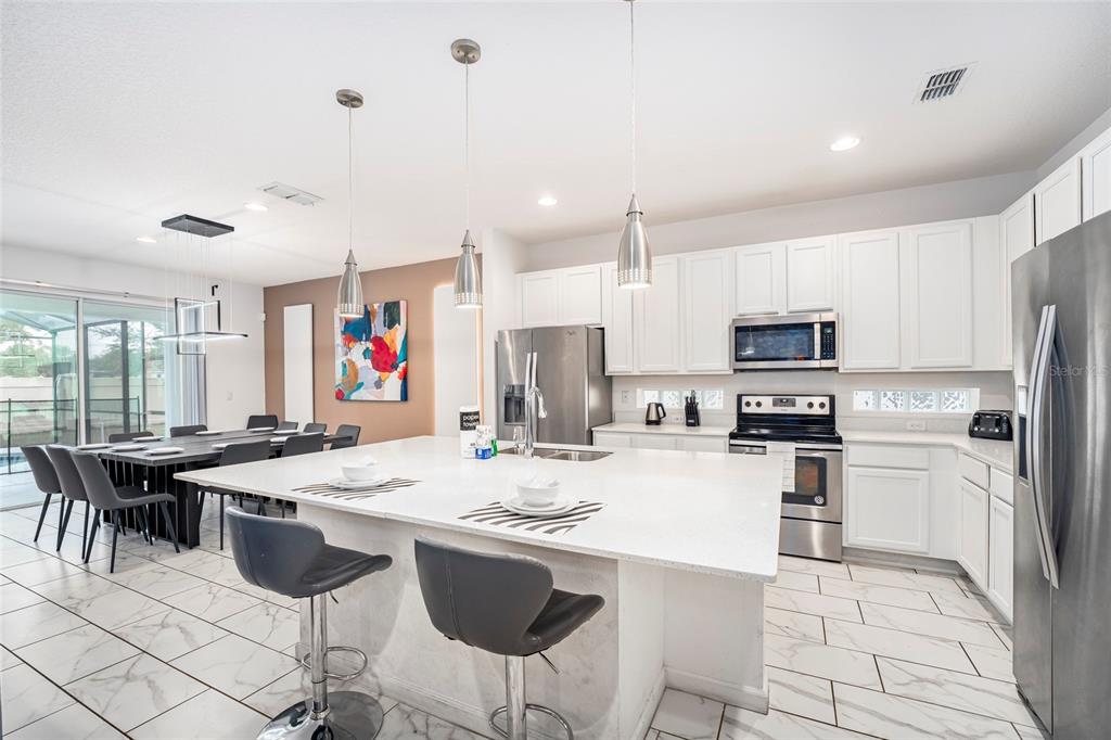 A modern kitchen features a large white quartz island, stainless steel appliances, and white cabinetry — 2613 CALISTOGA AVENUE, KISSIMMEE, FL
