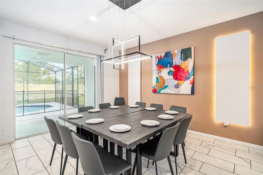 A dining room features a large wooden table, modern light fixture, and sliding glass doors — 2613 CALISTOGA AVENUE, KISSIMMEE, FL
