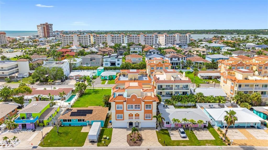 An aerial view shows a multi-story orange building surrounded by residential homes and palm trees — 146 175TH TERRACE DRIVE E, REDINGTON SHORES, FL