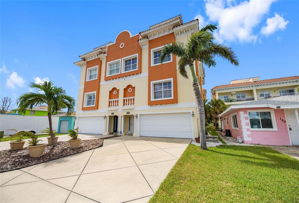 A three-story orange and cream townhouse features a concrete driveway and a palm tree — 146 175TH TERRACE DRIVE E, REDINGTON SHORES, FL