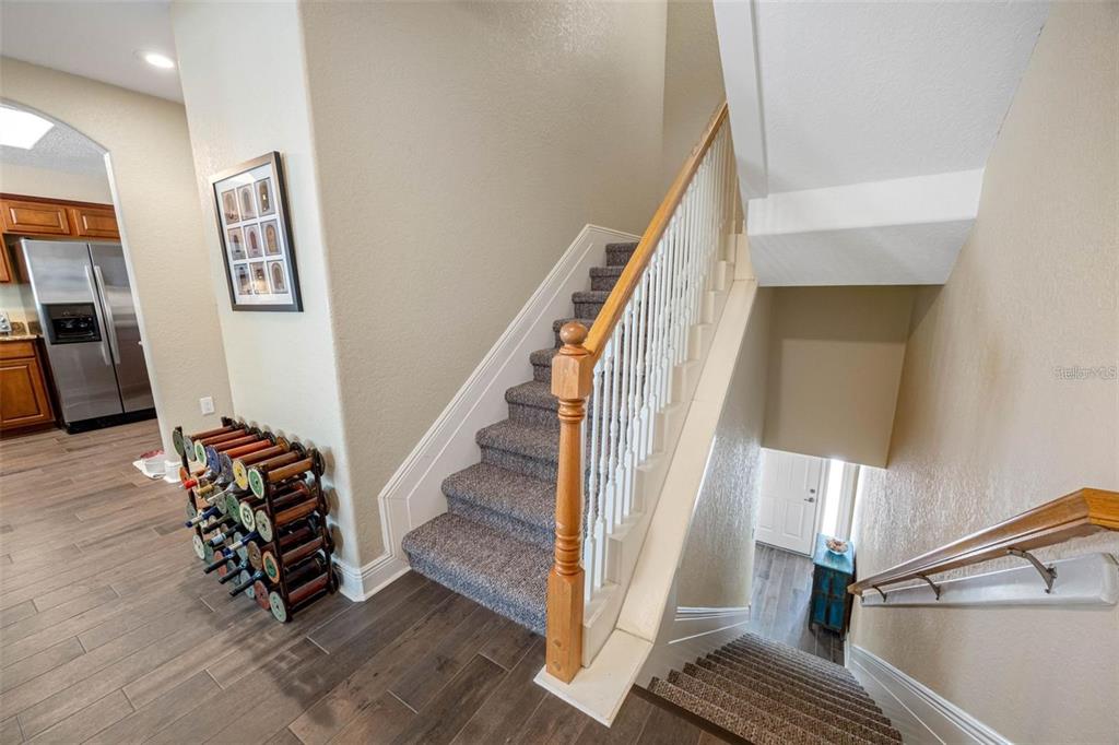 A carpeted staircase with a wooden railing leads to an upper level near a kitchen — 146 175TH TERRACE DRIVE E, REDINGTON SHORES, FL