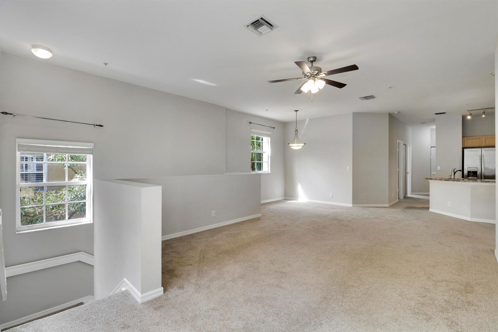 An open-concept living area features beige carpeting, neutral walls, a ceiling fan, and a kitchen — 104 Lighthouse Circle # H, Tequesta FL 33469, TEQUESTA, FL