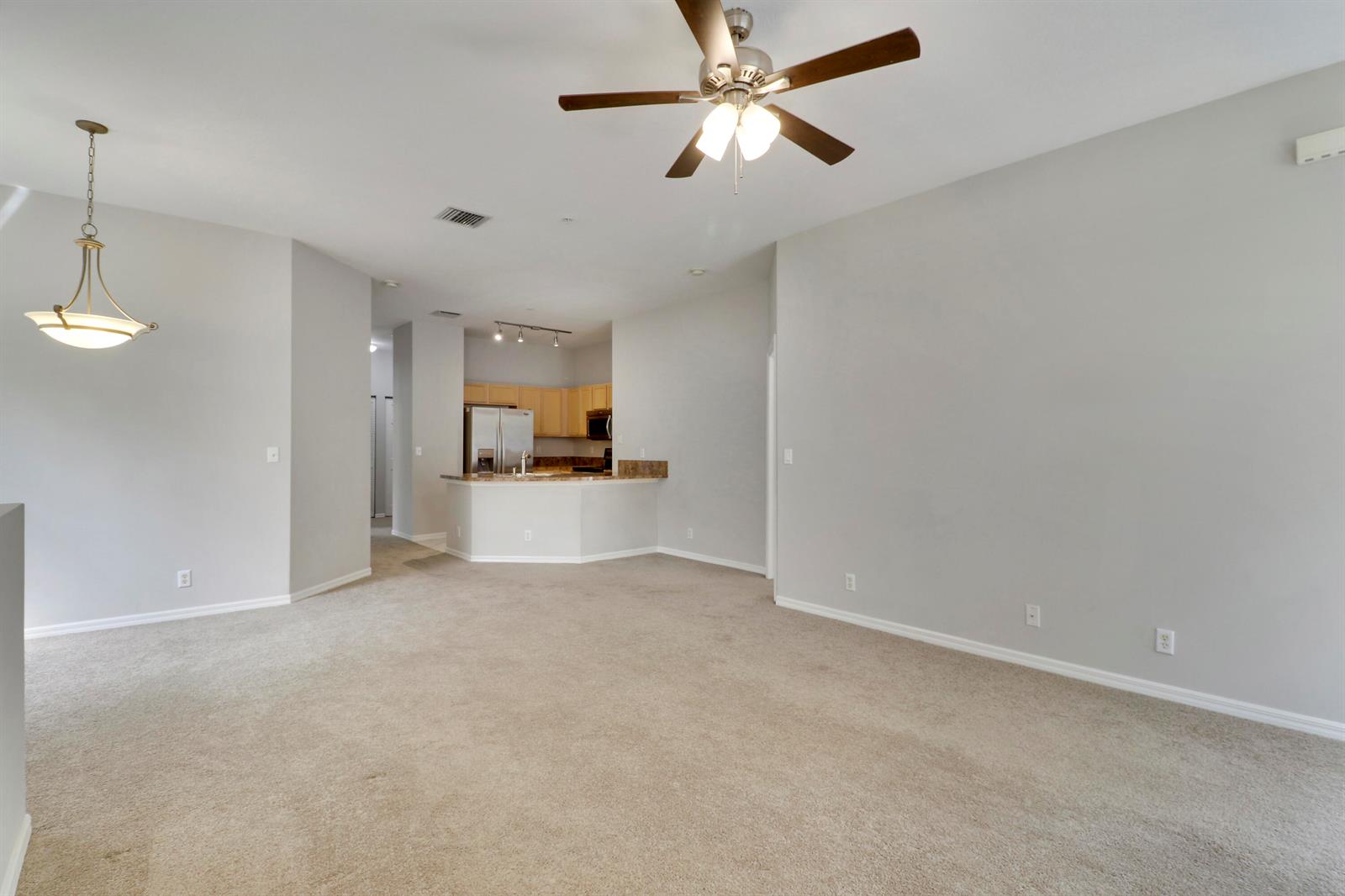 An open-concept living room with beige carpet, light gray walls, and a ceiling fan — 104 Lighthouse Circle # H, Tequesta FL 33469, TEQUESTA, FL