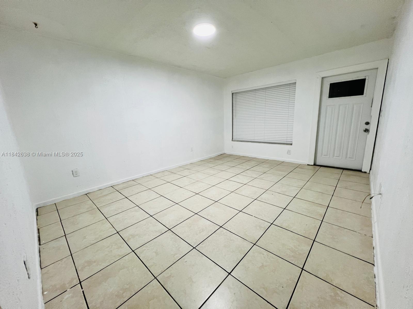 An empty room features white walls, light-colored tile flooring, a window with blinds, and a door — 2019 COLMAR AVE, Sebring FL 33870, SEBRING, FL