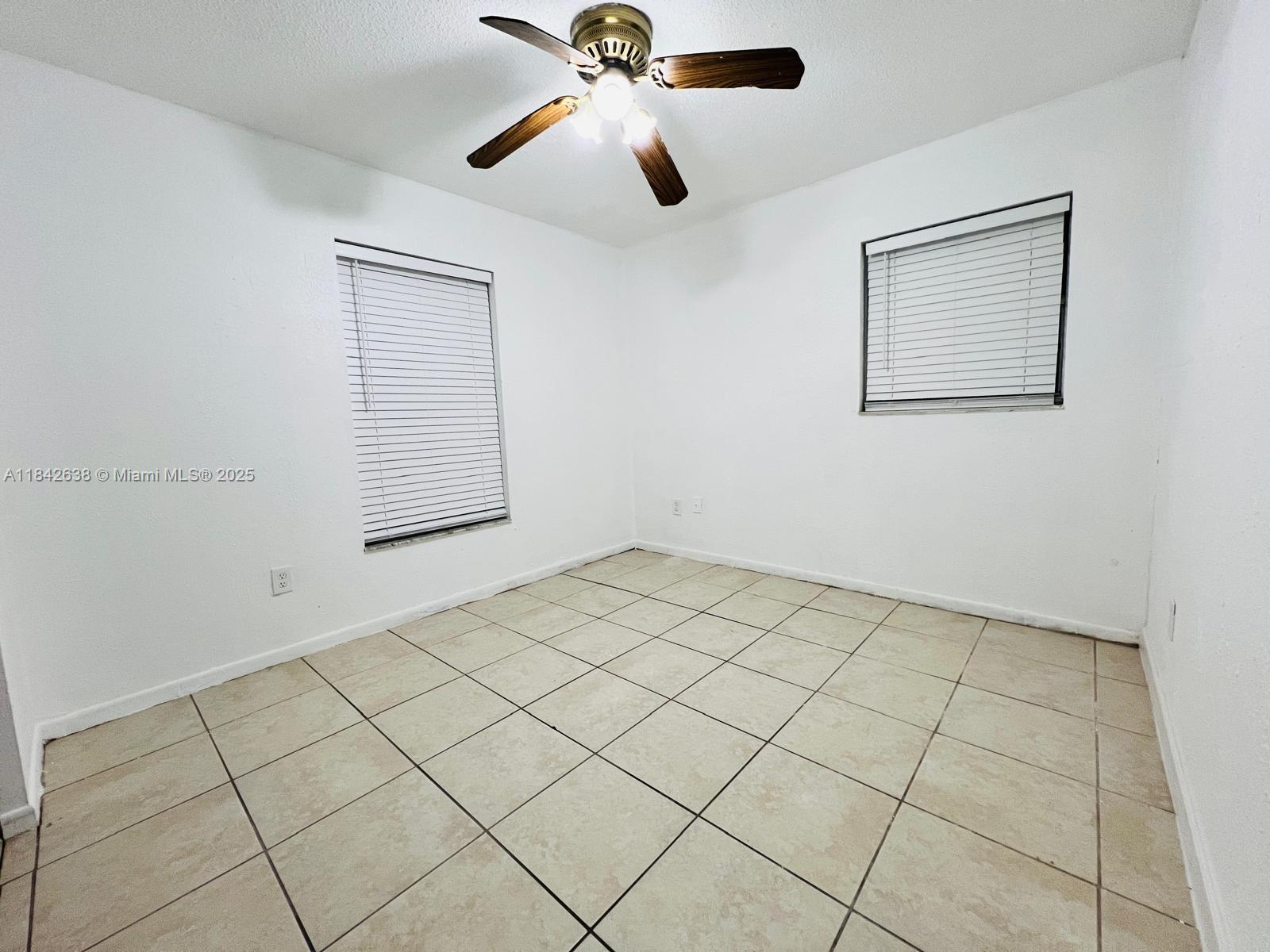 An empty room features white walls, tan tile flooring, two windows with blinds, and a ceiling fan — 2019 COLMAR AVE, Sebring FL 33870, SEBRING, FL