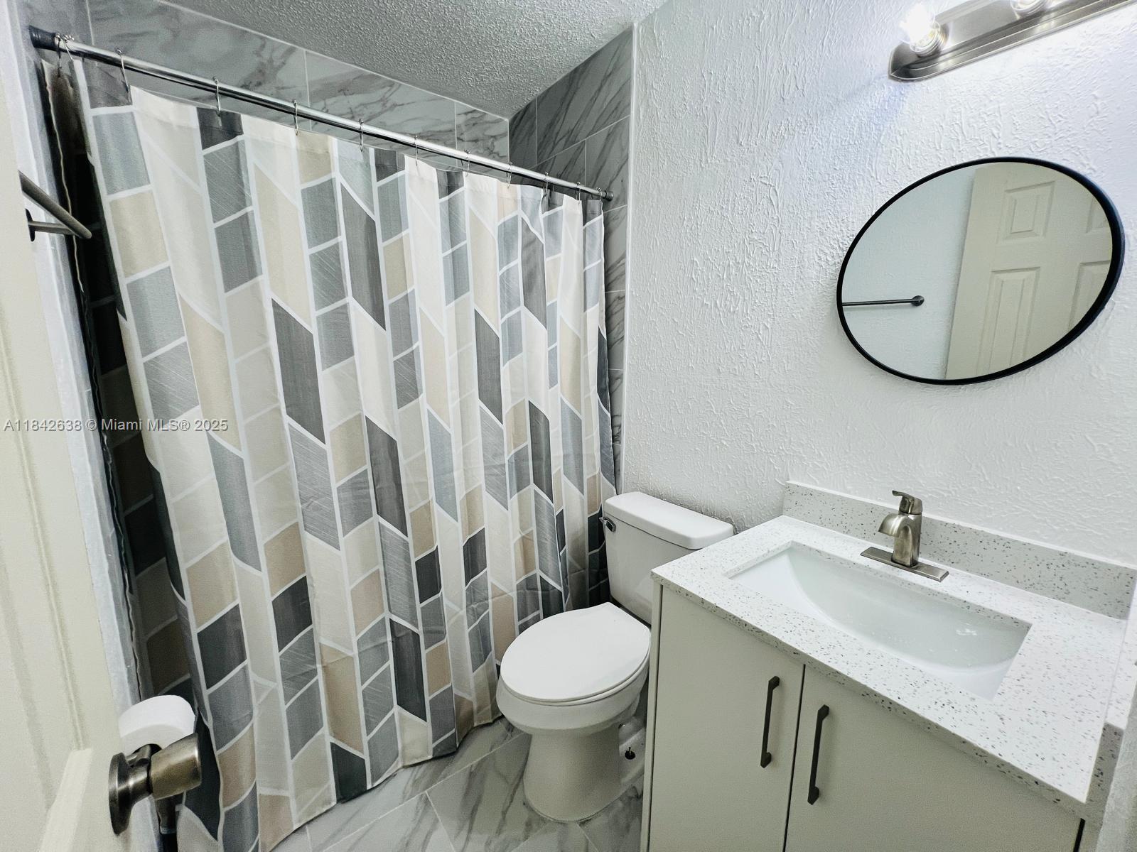A bathroom features a patterned shower curtain, a white vanity with a speckled countertop, and a mirror — 2019 COLMAR AVE, Sebring FL 33870, SEBRING, FL