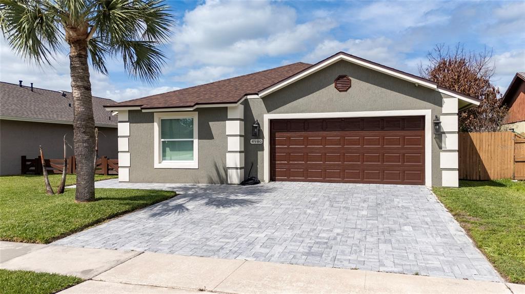 A single-story house with a gray stucco exterior, white corner accents, and a paved driveway — 4980 WARRIOR LANE, KISSIMMEE, FL