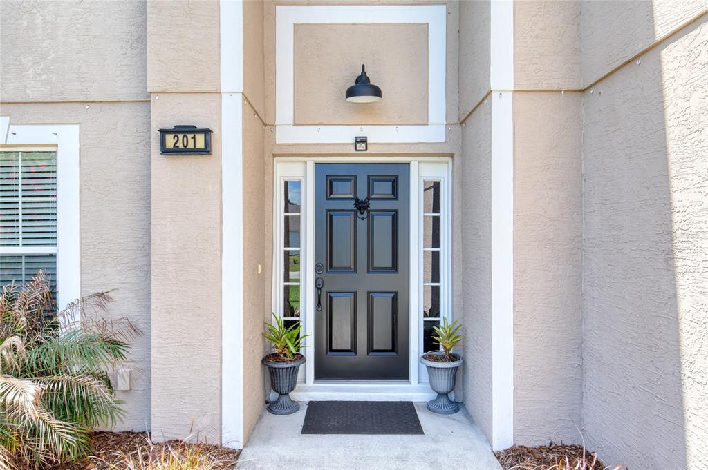 A black front door with sidelights is centered on the beige exterior of a house — 201 UNDERWOOD TRAIL, PALM COAST, FL