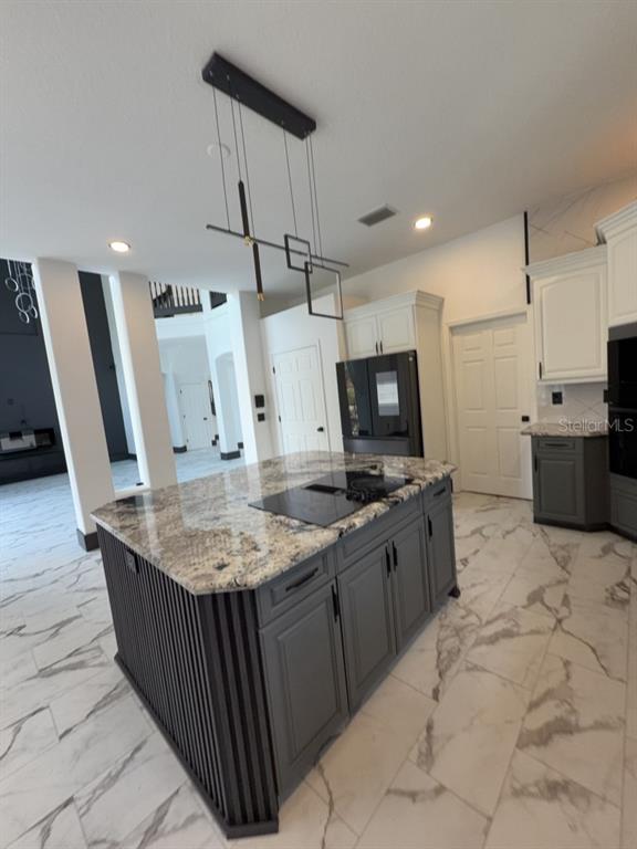 A kitchen features a large island with a cooktop, dark cabinetry, and marble-patterned tile flooring — 8131 VINELAND OAKS BOULEVARD, ORLANDO, FL