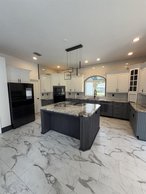 A kitchen features white and dark gray cabinetry, a marble-topped island, and marble-patterned tile flooring — 8131 VINELAND OAKS BOULEVARD, ORLANDO, FL