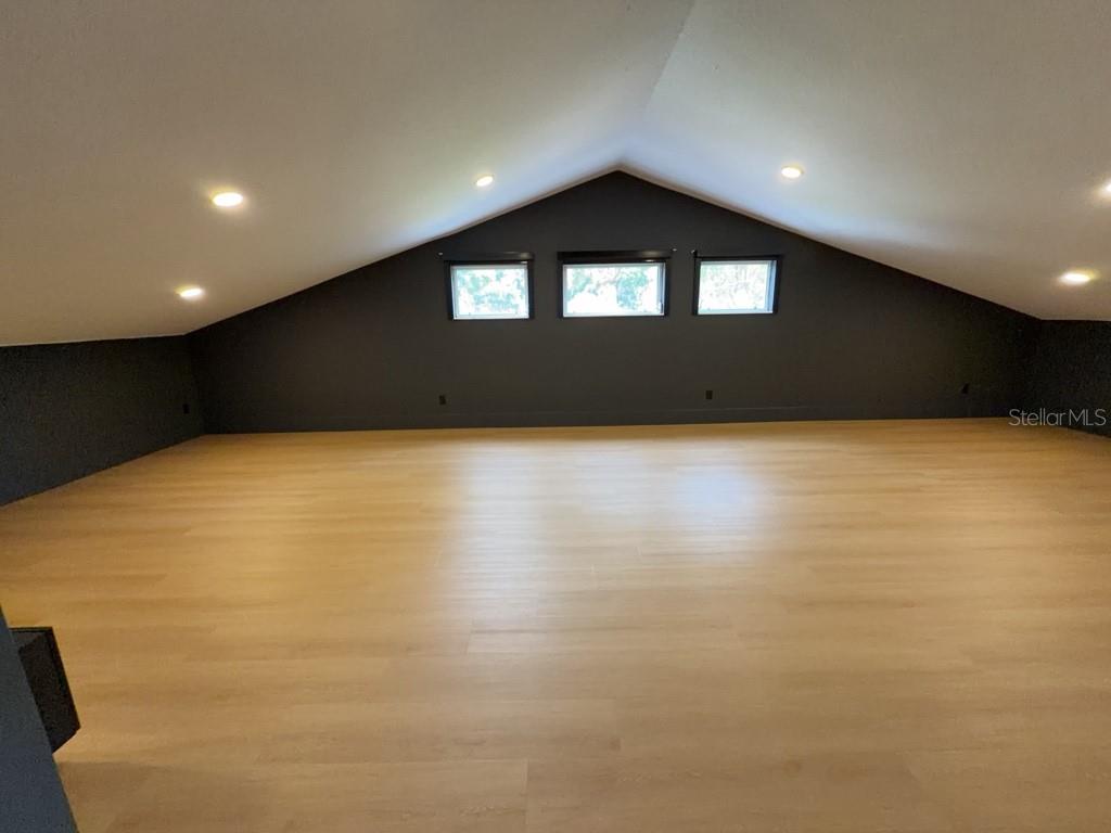 An attic room features light wood flooring, dark walls, and three windows under a vaulted ceiling — 8131 VINELAND OAKS BOULEVARD, ORLANDO, FL