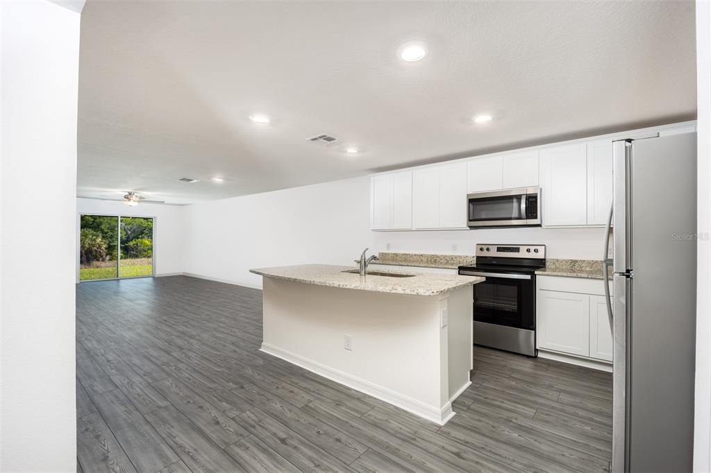 A kitchen with white cabinets, granite countertops, and stainless steel appliances opens to a living area — 3180 SEVILLE STREET, LAKE ALFRED, FL