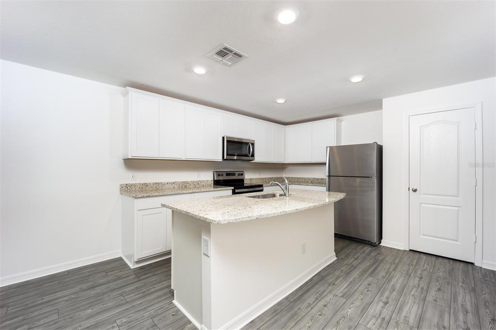 A kitchen features white cabinets, granite countertops, a center island, and stainless steel appliances — 3180 SEVILLE STREET, LAKE ALFRED, FL