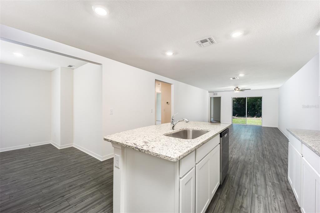 A kitchen island with a granite countertop and sink sits in an open-concept living space — 3180 SEVILLE STREET, LAKE ALFRED, FL